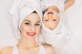 Smiling mother and daughter lying on white background, bathtime concept. Pretty young woman with little girl wearing