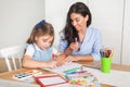 Smiling mother and daughter preparing for lessons and draws at the table with pencils and paints. Parent and pupil of preschool.