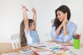 Smiling mother and daughter preparing for lessons and draws at the table with pencils and paints. Parent and pupil of preschool.