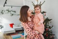 Smiling mother and daughter standing in front of the Christmas tree, mom holding her baby girl looking at her Royalty Free Stock Photo