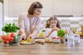 Smiling mother and daughter 8, 9 years old cooking together in kitchen vegetable salad. Healthy home food, communication parent