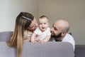 Smiling mother and father holding their baby girl daughter sitting on bed at home. Happy family concept, Bearded man in Royalty Free Stock Photo