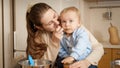 Smiling mother feeding her little baby with fruit puree on kitchen table. Concept of little chef, children cooking food, healthy Royalty Free Stock Photo