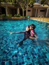 A happy mother holds her darling little girl as they stand side by side in a swimming pool.