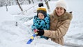 Smiling mother and her baby son cleaning snow from their car with a brush after a blizzard on a parking lot. The concept of daily Royalty Free Stock Photo