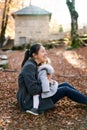 Smiling mother hugging little girl on her knees while sitting on leaves in autumn park Royalty Free Stock Photo