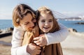 A smiling mother hugs her cute laughing daughter on the seashore. A young woman puts on a warm coat for her child on the beach