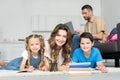 smiling mother and kids looking at camera while doing homework together and man Royalty Free Stock Photo
