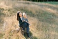 Smiling mother with a little girl on her knees sits on a stone in a sunny meadow Royalty Free Stock Photo