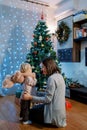 Smiling mother with a little girl with a teddy bear on her shoulders, sits near the Christmas tree Royalty Free Stock Photo