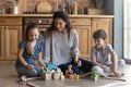 Smiling mother and little siblings playing colorful wooden blocks