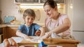 Smiling mother with little son powdering wooden board with flour for rolling biscuits dough. Children cooking with