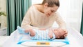 Smiling mother looking and stroking her little son while weighing him on digital scales on changing table at home Royalty Free Stock Photo