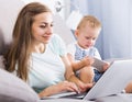 Smiling mother is productively working behind laptop while kid playing on tablet Royalty Free Stock Photo