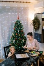 Smiling mother with rolling pin looking at little daughter examining cookies on tray