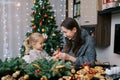Smiling mother showing little girl berries for Christmas wreath while sitting at table