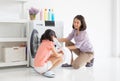 Smiling mother sitting looking at her cute daughter helping her loading clothes into a washing machine in a laundry room at home. Royalty Free Stock Photo