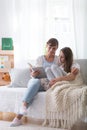 Smiling mother and teenager daughter sitting on the couch, reading book together Royalty Free Stock Photo