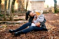 Smiling mother tickling little girl on her lap while sitting on fallen leaves in the park Royalty Free Stock Photo