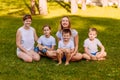 Smiling mothers and children sit on the green grass. Big happy family, two women and three children in white t-shirts Royalty Free Stock Photo