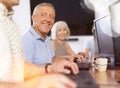 Smiling motivated older man using computer at internet cafe