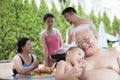 Smiling multi-generational family barbequing by the pool on vacation