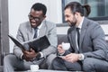 smiling multicultural business partners reading document and drinking coffee