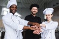 smiling multicultural chefs putting hands together