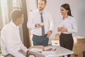 smiling multiethnic colleagues talking and looking at each other during coffee break in new Royalty Free Stock Photo