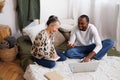 Smiling young multiethnic couple talking while using laptop during online education on bed Royalty Free Stock Photo