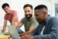 Smiling multiracial male coworkers looking at businessman working over laptop in office Royalty Free Stock Photo