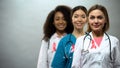 Smiling multiracial nurses with pink ribbons, international breast cancer sign