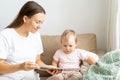 Smiling mum reading book with curious toddler on couch in living room. Horizontal natural light Royalty Free Stock Photo