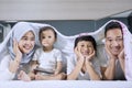 Smiling Muslim family lying under a blanket