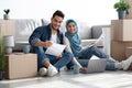 Smiling muslim family sitting on floor with laptop among boxes Royalty Free Stock Photo