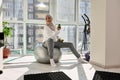 Smiling muslim girl in hijab exercising with dumbbells at home, looking away while sitting on a fit ball Royalty Free Stock Photo