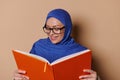 Smiling Muslim Woman Wearing Eyeglasses And Hijab, Reading Book On Beige Background. Erudite And Educated People Concept