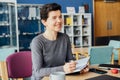 Smiling neutral gender middle-aged person making notes in paper notebook, using laptop, working in open space office Royalty Free Stock Photo