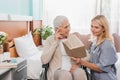 smiling nurse reading book to senior patient with hearing aid sitting Royalty Free Stock Photo