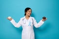 Smiling nutritionist in medical gown an blue ribbon holding a bowl with refined white sugar in one hand and ripe sweet dates in