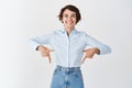 Smiling office ceo woman in blue collar shirt, pointing fingers down at company name and looking happy, standing on Royalty Free Stock Photo