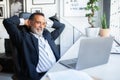 Smiling old caucasian man in suit resting, looking at laptop at table in office interior Royalty Free Stock Photo