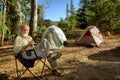 Smiling old hiker in the camp in morning forest