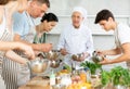 Smiling old man chef of cooking course teaching attendees how to mix sauce