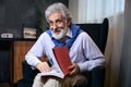 Smiling old man is sitting in a cozy armchair with a book Royalty Free Stock Photo