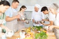 Smiling old man chef of cooking course teaching attendees how to mix sauce