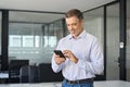 Smiling older business man executive standing in office using mobile phone. Royalty Free Stock Photo