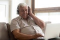 Smiling older man wearing wireless headphones enjoying music, using laptop Royalty Free Stock Photo