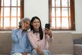 Smiling older mother and adult daughter using phone together, sitting on cozy sofa at home, happy young woman and mature Royalty Free Stock Photo