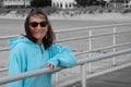 Smiling older woman in color with her arm on a boardwalk fence rail with the beach and fence in black and white Royalty Free Stock Photo